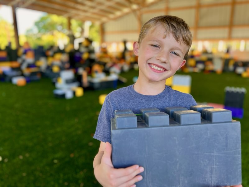 A young boy holding a building block cheerfully in a play area at Camp Impact