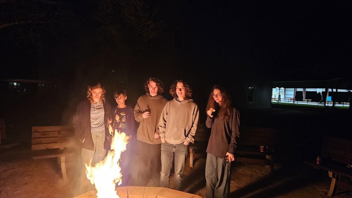 Five teenagers standing together behind a glowing campfire at night